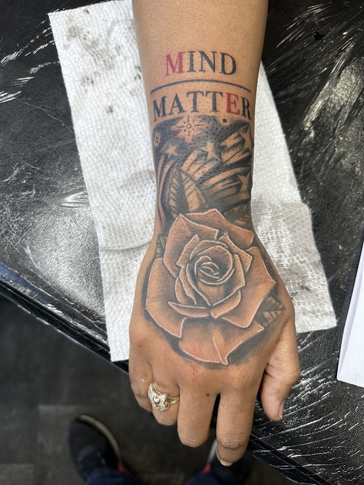 Black and gray rose tattoo on a hand with Mind Over Matter lettering on the forearm