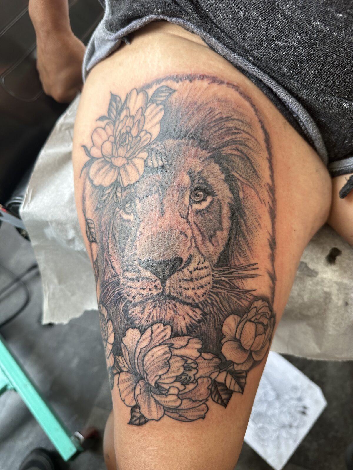 Black and gray lion head with floral elements tattoo on an upper outer thigh