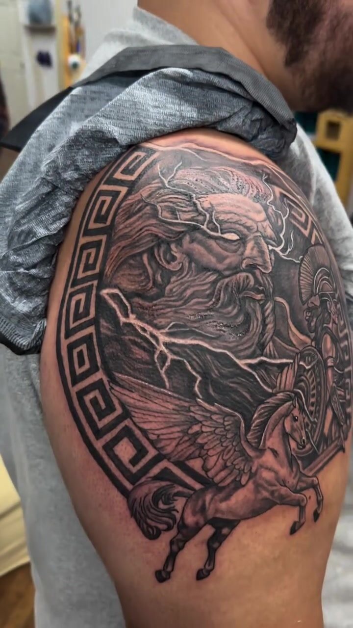 Black and gray Zeus with lightning and Pegasus in a Greek key border tattoo on a shoulder