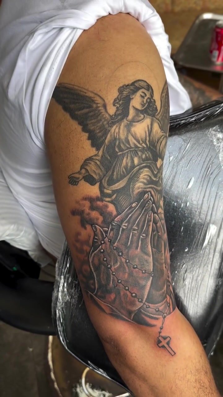 Black and gray angel with rosary tattoo on an upper arm